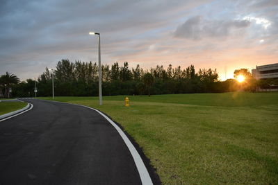 Street by trees against sky during sunset