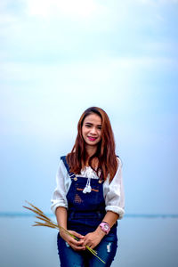 Portrait of smiling young woman standing against sky