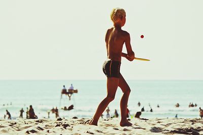 Teenage boy playing on beach against clear sky