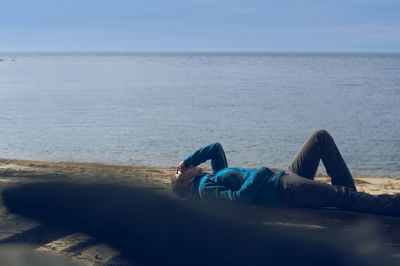 Man lying down on beach against blue sky