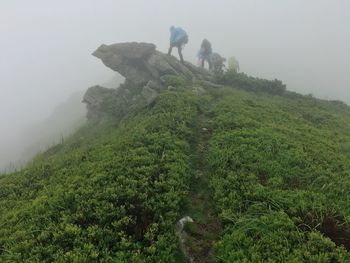 Rear view of people standing on mountain against sky during foggy weather