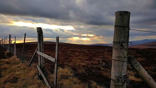 Fence on field against cloudy sky