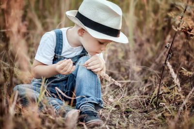 Cute boy sitting on field amidst plants