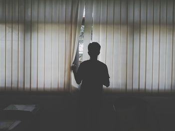 Rear view of man against blinds at home