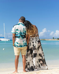 Rear view of a young couple standing at beach while looking toward the horizon