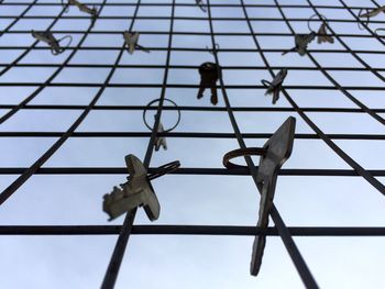 Low angle view of keys hanging on chainlink fence against sky