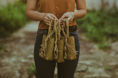 Midsection of woman holding wicker bags while standing outdoors