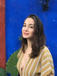 Portrait of smiling young woman standing against blue wall