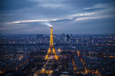 Illuminated buildings in city against cloudy sky