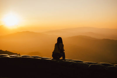 Rear view of woman sitting against sky during sunset