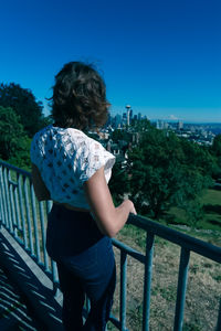 Woman standing by railing against clear blue sky