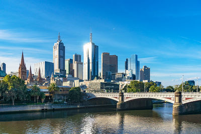 Bridge over river by buildings in city against sky