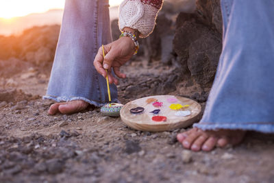 Low section of woman painting stone while sitting on rock