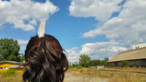 Rear view of woman wearing feather in ponytail against cloudy sky