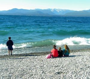 Rear view of people sitting on beach against sky