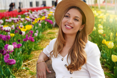 Smiling girl sitting relaxed between tulips fields on sunset. looking to the side.