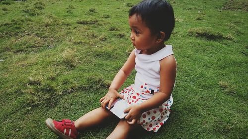 Cute girl with mobile phone sitting on grassy field