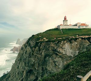 Lighthouse on rock by building against sky