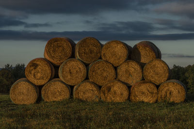 Stack of hay bales on field against sky