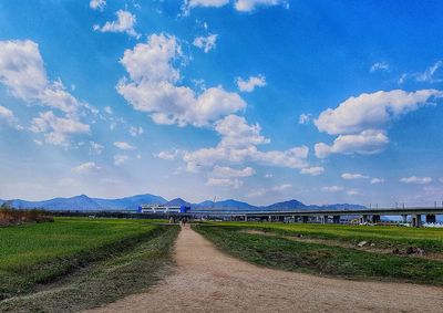 Road amidst field against blue sky