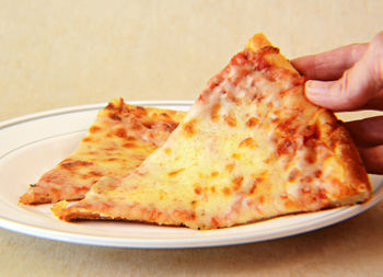 Cropped hand of woman holding pizza slice in plate on table