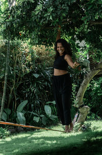Smiling young woman standing on rope against trees