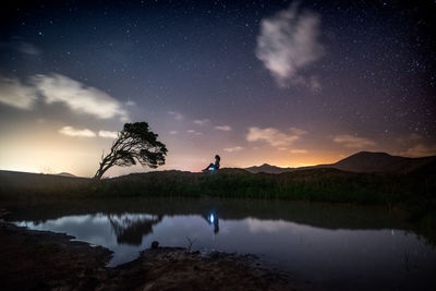Reflection of man in lake against sky at night