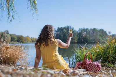 Beautiful caucasian woman in yellow dress on a picnic outdoors, sitting next to water