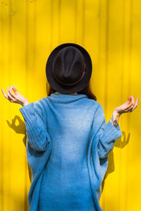 Rear view of person wearing hat standing against yellow wall