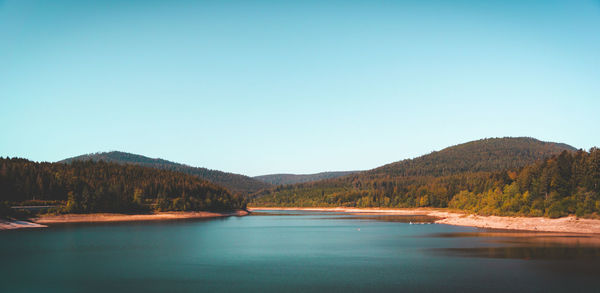 Scenic view of lake by mountains against clear blue sky