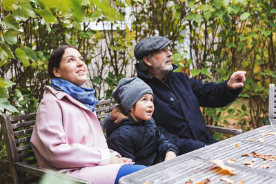 Senior man gesturing while sitting with great grandson and daughter at wooden table in park