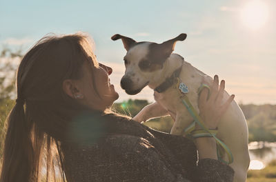 Young woman in autumn outfit holding her dog and embracing him. hugging loving pet in a park