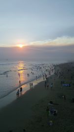 People on beach against sky during sunset