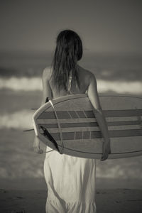 Rear view of woman standing at beach against sky