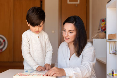 Mother assisting son in puzzle sitting at home