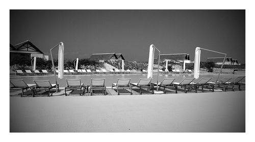 Empty chairs by swimming pool against clear sky