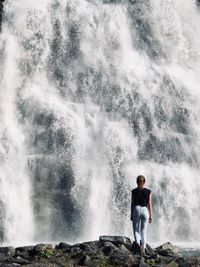 Rear view of woman standing against waterfall