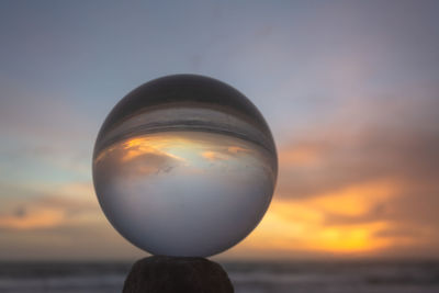 Close-up of crystal ball on rock against sky during sunset