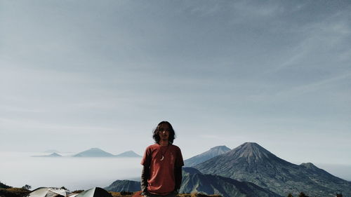 Woman sitting on mountain against sky