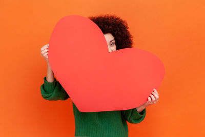 Midsection of woman holding heart shape against yellow background
