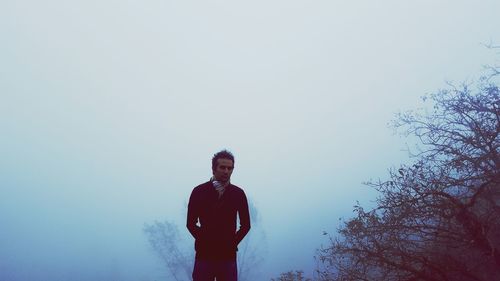 Man standing by bare tree during foggy weather