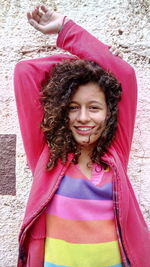 Portrait of smiling girl with arms raised standing against wall