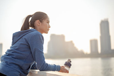 Side view of woman with arms raised against city in background