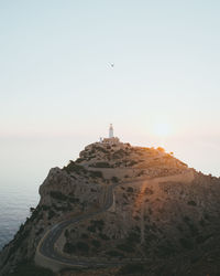 Lighthouse on mountain against sea during sunset