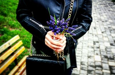 Midsection of woman holding bouquet against purple wall