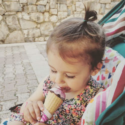 Close-up of cute girl licking ice cream against stone wall