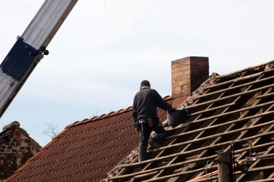 Rear view of men working on roof of building against sky