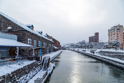Frozen river in city against sky during winter