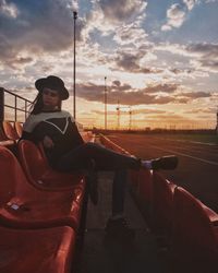 Woman sitting on chair in stadium against sky during sunset