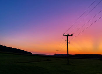 Silhouette electricity pylon on field against romantic sky at sunset